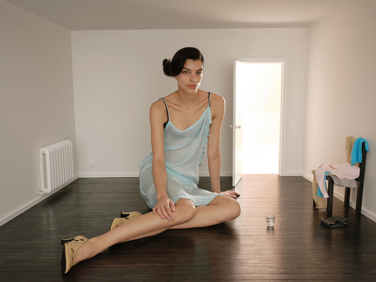 Model in a pale blue Paloma Wool dress seated on a dark floor