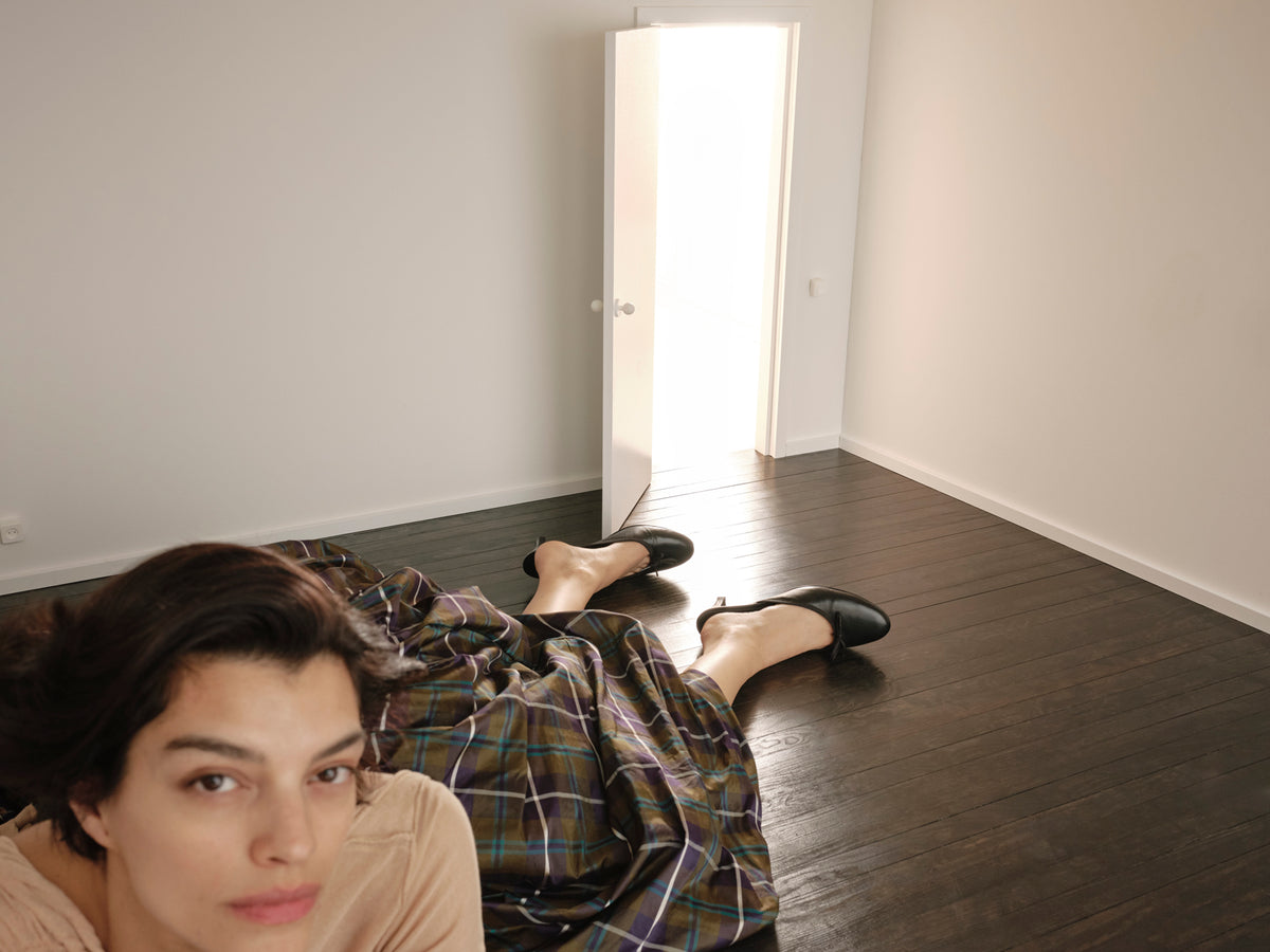 Model wearing a voluminous checked skirt lying diagonally across a room